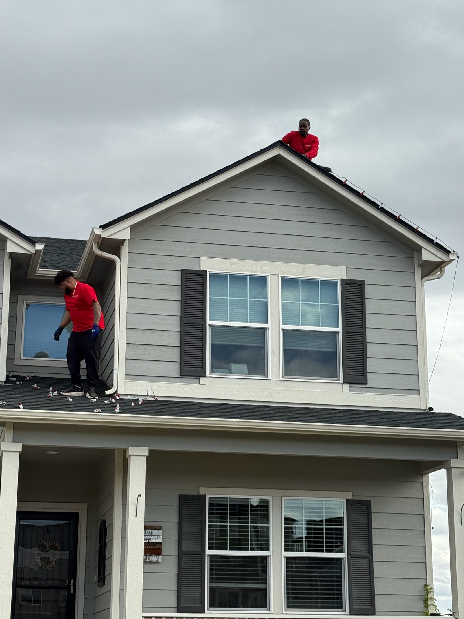Our installers on roof peak hanging holiday lights on a gray two-story house