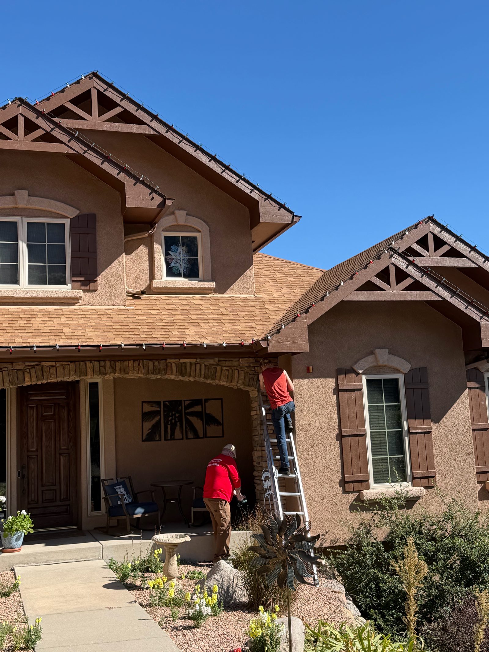 Our Front Range crew on ladder installing roofline Christmas lights by the front porch
