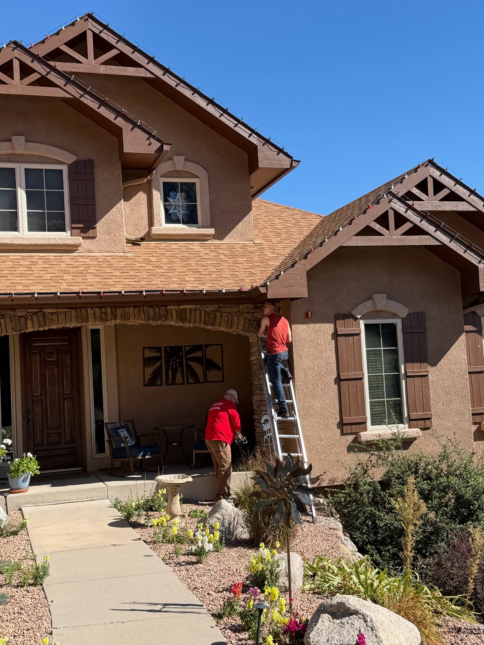 Christmas light installers on ladder hanging red Christmas lights on a Front Range home